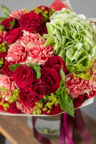 Röda och gröna blommor. Höstbukett av blandade blommor i glasvas på träbord. Blomsterhandlarens arbete i en blomsteraffär. Färsk snittblomma. — Stockfoto