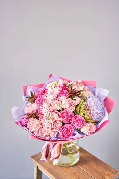 Bouquet viola e rosa con il fiore del carciofo. Bellissimi fiori sul tavolo di legno. Concetto di fioritura. Colori primaverili. il lavoro del fioraio in un negozio di fiori. — Foto Stock