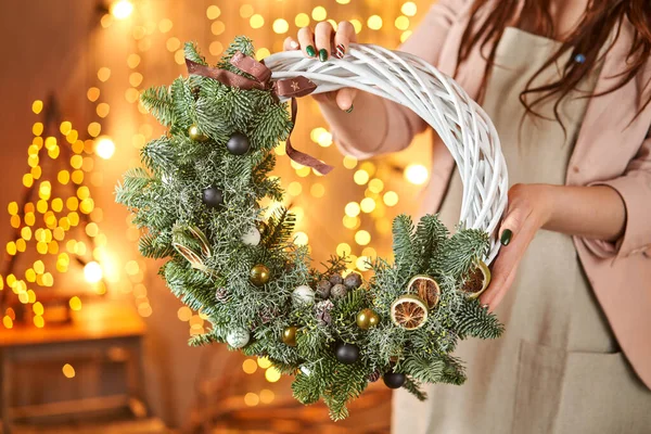 Noel çelengi tutan genç bir kadın Noel için köknar dalları ve Noel oyuncakları süslüyor. Yeni yıl kutlaması. Avrupa çiçek dükkanı — Stok fotoğraf