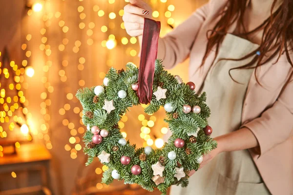 Jovem segurando um laço de grinalda de Natal decorado ramos de abeto e brinquedos de Natal para o feriado. A celebração do ano novo. Loja de flores europeia — Fotografia de Stock