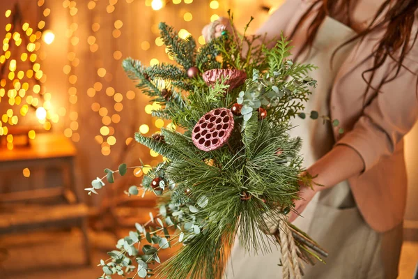 Jovem segurando uma coroa de Natal-loop ramos de abeto decorados e brinquedos de Natal para o feriado. A celebração do ano novo. Loja de flores europeia — Fotografia de Stock