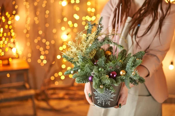 Bayram için elinde köknar dalları olan metal bir Noel kovası tutan genç bir kadın. Yeni yıl kutlaması. Avrupa çiçek dükkanı — Stok fotoğraf