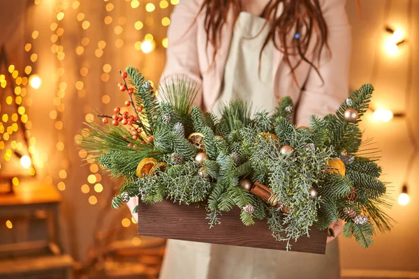 Jovem segurando uma caixa de madeira de Natal com ramos de abeto para o feriado. A celebração do ano novo. Loja de flores europeia — Fotografia de Stock