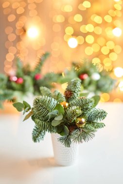Norveç çam nobilisi ile Noel düzenlemesi ve bir seramik kupasında Noel dekoru ile süslenmiş. Arka planda çelenk var. Noel aşkı. Koyu ahşap masa karla kaplanmış.