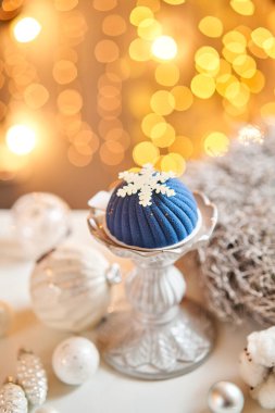 Fonda mavi kadife lambalarla kaplı mini kremalı pasta. Bokeh arka planda. Modern Avrupa pastası. Fransız mutfağı. Noel teması