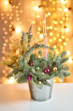 Norveç çam nobilisi ile noel düzenlemesi ve metal bir kupayla süslenmiş Noel süsü. Arka planda çelenk var. Noel aşkı. Koyu ahşap masa karla kaplanmış.