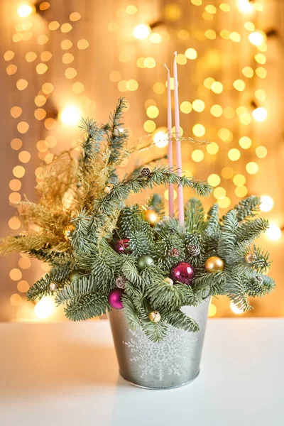 Accordo natalizio con pino norvegese Nobilis e decorato con decorazioni natalizie in una tazza di metallo. Garland Bokeh sullo sfondo. Amore natalizio. Tavolo in legno scuro cosparso di neve — Foto Stock