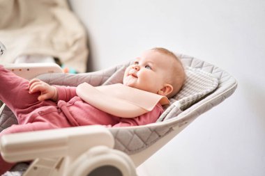 Genç anne bebeğini meyve püresiyle besliyor. Bebek 7 aylık, bebekler için özel bir sandalyede yatıyor..