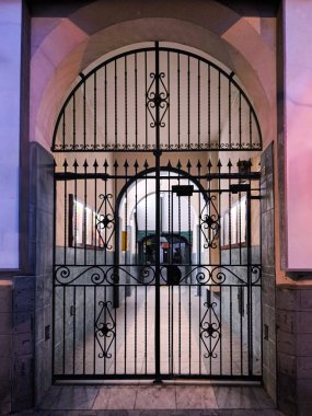 İşlenmiş demir kapı ve yumuşak ışıklandırmalı, sıcak ve zarif bir atmosfer yaratan tarihi kemerli bir giriş..