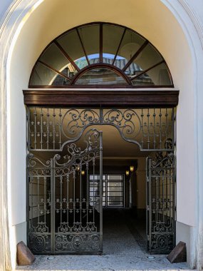 Mimari bir kemerin altında, üst kattaki camda klasik Avrupa binalarının yansımaları olan zarif dövmeli demir kapı..