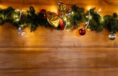 Mücevherleri, altın yayı ve ahşap bir duvarda asılı sıcak peri ışıklarıyla Noel çelengi, metin için boş fotokopi alanı olan şenlikli tatil arka planı.