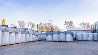 Mavi gökyüzünün altındaki bir sanayi deposunda muşamba kaplı büyük beyaz torbalar, lojistik, inşaat malzemeleri ve toptan mal depolamayı simgeliyor..