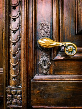 Süslü bir pirinç sapı ve oyulmuş detayları olan eski bir ahşap kapıya yakın plan, ahşap tahılı, giriş konseptini, güvenliği, tarihi mimariyi vurgulayan sıcak ışık,