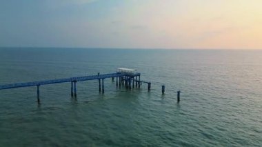 A serene drone shot of Jetty Ghat in Coxs Bazar during sunset, capturing calm waves, golden light, and the peaceful seaside atmosphere of the worlds longest natural sea beach.