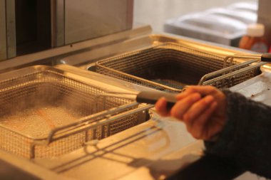 A close-up, action-filled shot of hands operating an industrial deep fryer as churros cook in vigorously boiling oil