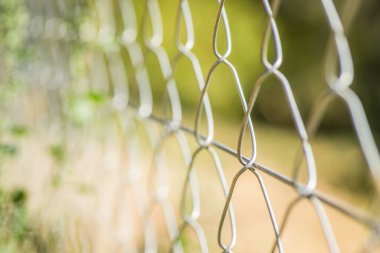 Beton sütunlarda örülmüş tel örgüler. Arka planda yeşil çimenler olan tel çitler.