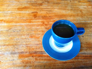 İçi sıcak siyah kahve dolu mavi bir kupa içeren ahşap masa. Mesaj veya tırnak içinde boşluk kopyala. Rahatlatıcı bir an ve günün tadını çıkarıyor..