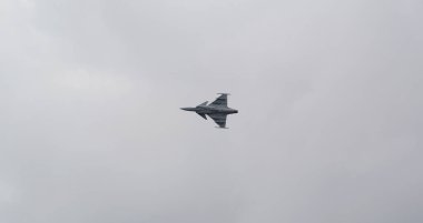 Güçlü bir jet uçağı Polonya 'nın Leszno kentindeki bir hava gösterisi sırasında akrobatik manevralar yapıyor. Gri gökyüzü uçakların hızını ve motor gücünü vurguluyor.