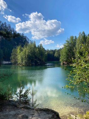 Sakin bir zümrüt göl, yüksek uçurumlar ve sık ormanlar tarafından çerçevelenir, manzarayı yansıtır ve uyumlu bir doğal manzara yaratır..
