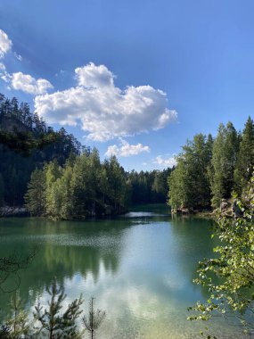 Sakin bir zümrüt göl, yüksek uçurumlar ve sık ormanlar tarafından çerçevelenir, manzarayı yansıtır ve uyumlu bir doğal manzara yaratır..