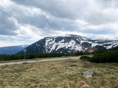 Karlı Karkonosze Dağları 'nın panoramik bir görüntüsü, beyaz kar parçalarının, dağ patikasının üstündeki dramatik bulutlu gökyüzünün altında koyu kayalık yamaçlarla tezat oluşturduğu yer..