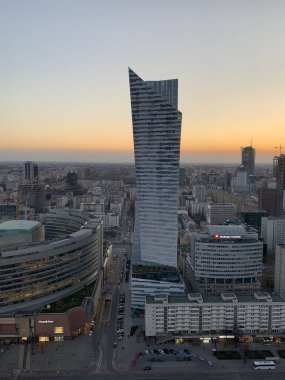 Günbatımında Varşova 'nın merkezinde modern bir gökdelen, ofis binaları, yollar ve yoğun kentsel gelişim ile çevrili..