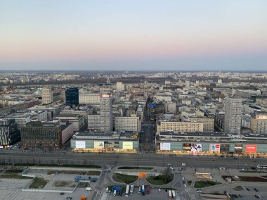 Gün batımında Varşova 'nın merkezinin panoramik görüntüsü: şehir blokları, modern binalar ve ufka doğru uzanan geniş yollar.