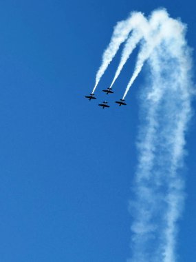 Dört akrobatik uçak, Polonya 'nın Leszno kentindeki bir hava gösterisinde açık mavi gökyüzünde duman izi bırakarak senkronize bir manevra gerçekleştiriyor. Kopya alanı ile dinamik hava performansı