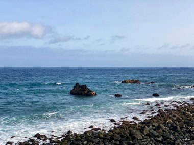 Tenerife 'nin kayalık kıyıları boyunca Atlantik Okyanusu, Kanarya Adaları. Volkanik taşlarla sakin deniz manzarası, yumuşak dalgalar, kıyı şeridi, ufuk çizgisi ve açık gün ışığı.