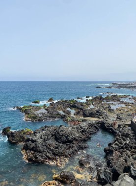 Tenerife, Puerto de la Cruz 'da Atlantik kıyısındaki doğal volkanik okyanus havuzları. Siyah lav kayaları, berrak su ve eşsiz bir kıyı manzarasında yüzen insanlar.