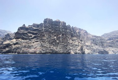 Kanarya Adaları 'ndaki Tenerife Adası' ndaki Masca Sahili boyunca devasa volkanik kayalıklar. Derin mavi Atlantik Okyanusu suyu ve dokunulmamış kıyı doğası dramatik bir doğal deniz manzarası yaratıyor..