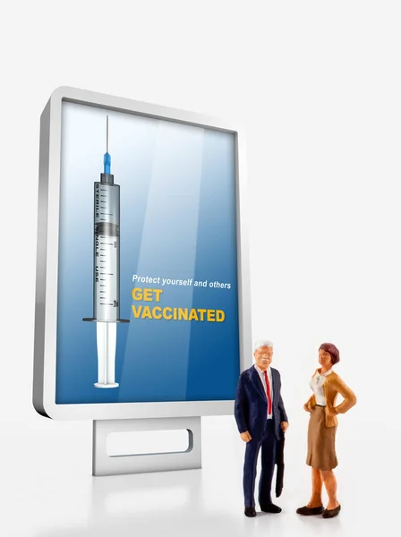 Miniature peoples about COVID-19, a group of different age people are standing in front of a billboard with a message to get vaccinated against covid-19
