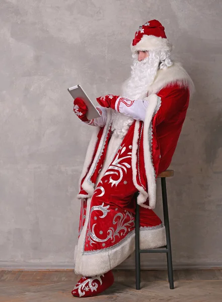 Father Frost looking at the tablet while sitting on chair — Stock Photo, Image