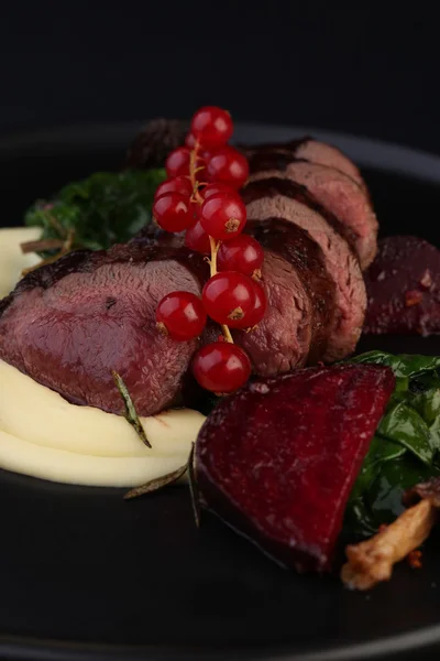 Heerlijke vlees-medaillons met saus en rode bessen op zwarte plaat — Stockfoto