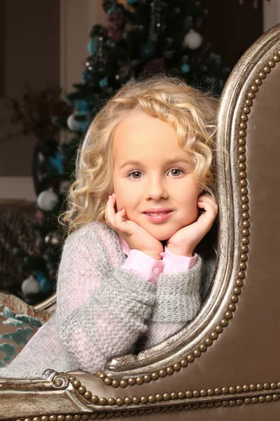 Cute little blond girl sitting peering over chair arms Stock Photo