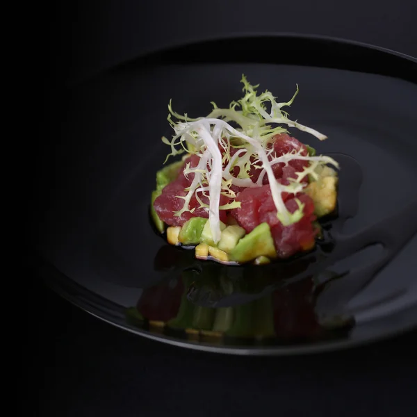 Smoked salmon, avocado, arugula and the sauce on black plate, dark background — Stock Photo, Image