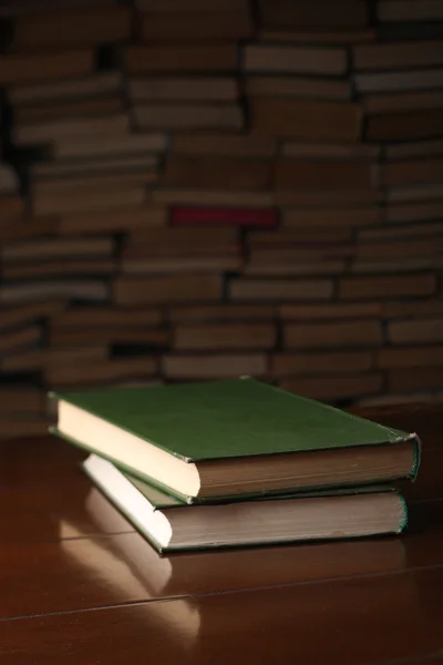 Two books are on the wooden table against background a number of books