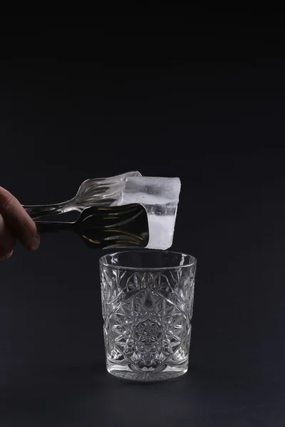 Glass with ice, hand on a dark background — Stock Photo, Image