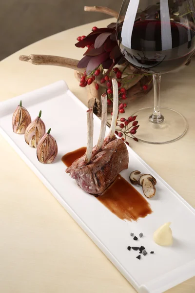 Bio-gegrillte Lammkoteletts mit Knoblauch und Soße auf einem weißen Teller der Hintergrund des Glases Rotwein, Blumen — Stockfoto