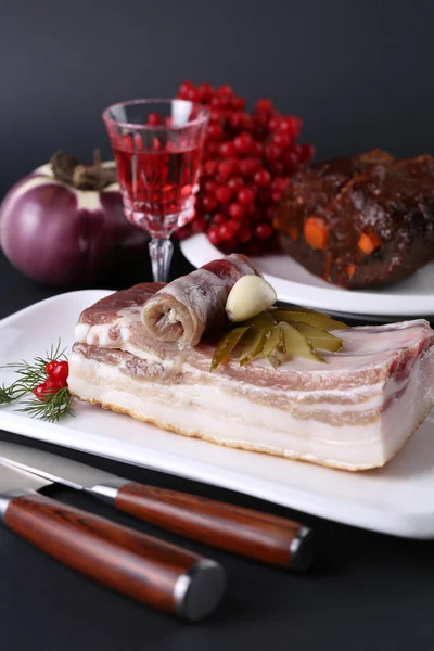 Bacon, cucumber and garlic on a white plate. Salty spiced lard, glass of drink with knifes, plate viburnum. Ukrainian cuisine — Stock Image Bacon, cucumber and garlic on a white plate. Salty spiced lard, glass of drink with knifes, plate viburnum. Ukrainian cuisine Stock Photo