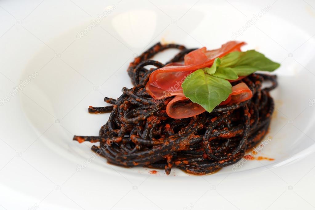 White plate of black spaghetti with red souse and greens