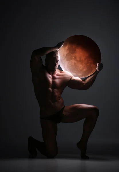 Young naked man with muscular body stands kneeling on floor — Stock Fotó