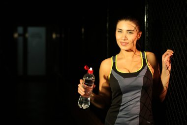 Young fitness girl with bottle of water on dark background
