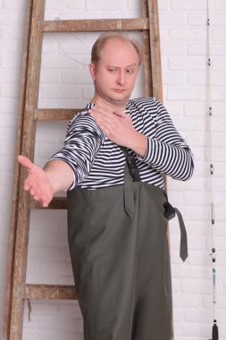 Fisherman shows hands the size of fish on white wall background.