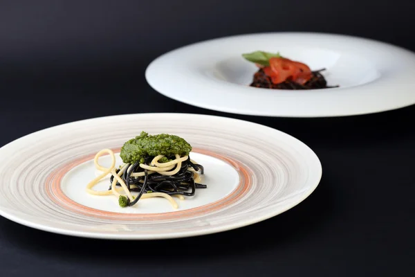 Two plates of black and white spaghetti with different sauces