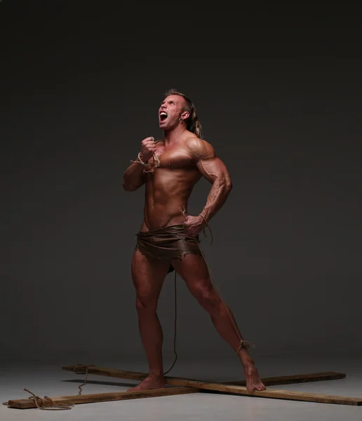 Кричащий голый мускулистый мужчина, руки связаны веревкой с деревянными балками — стоковое фото