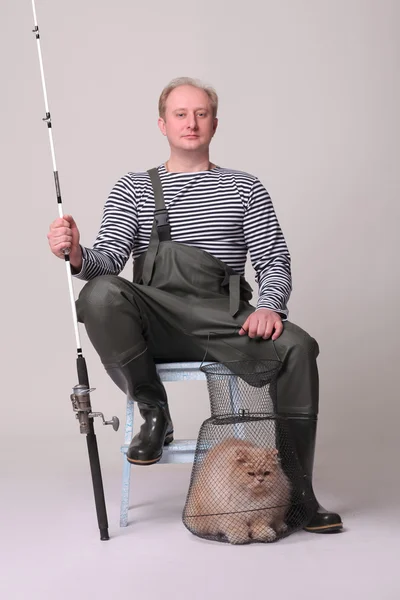 Pescador en vadeadores sentado en la silla, sosteniendo un equipo de pesca con gato — Foto de Stock