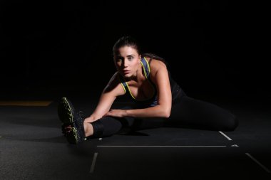 Young woman athlete sitting on the split, black background.