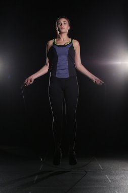 Cute, athletic girl with a skipping rope on black background.