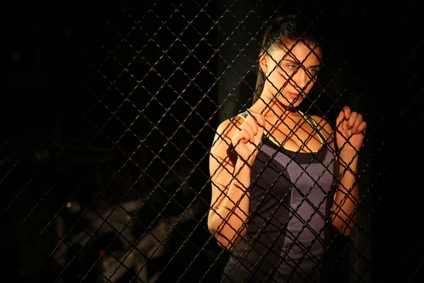 Portrait beautiful fitness girl near fence of grid in gym — Stock Photo, Image